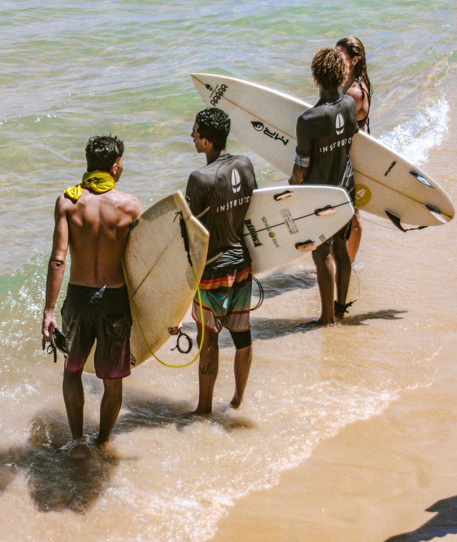 Grupo de surfistas juveniles caminando hacia el mar, acompañados por un instructor